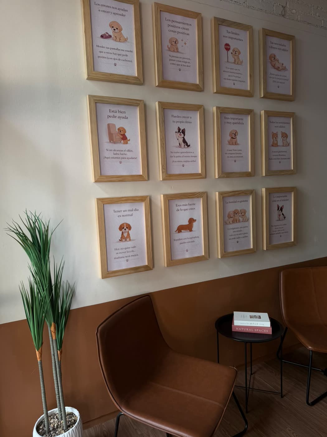 Muro de la sala de espera con doce cuadros enmarcados en madera clara; cada uno tiene una ilustración de cachorro y una afirmación en español.